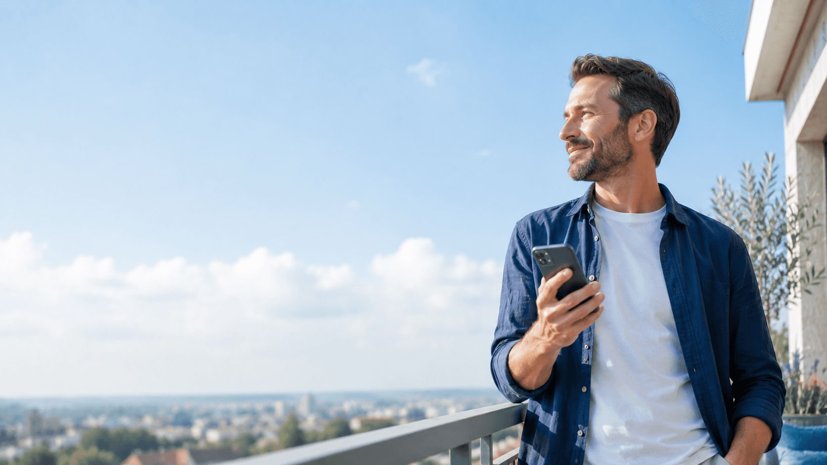 Homme sur un balcon ensoleillé face à la ville, smartphone à la main